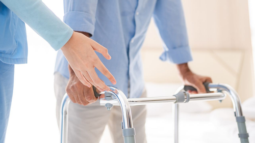 Un professionnel de la santé aide un homme à utiliser un déambulateur dans une chambre.