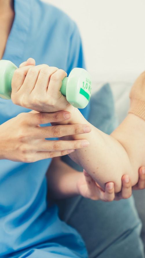 Un professionnel de la santé aide un patient à soulever un petit haltère vert pendant une thérapie physique.
