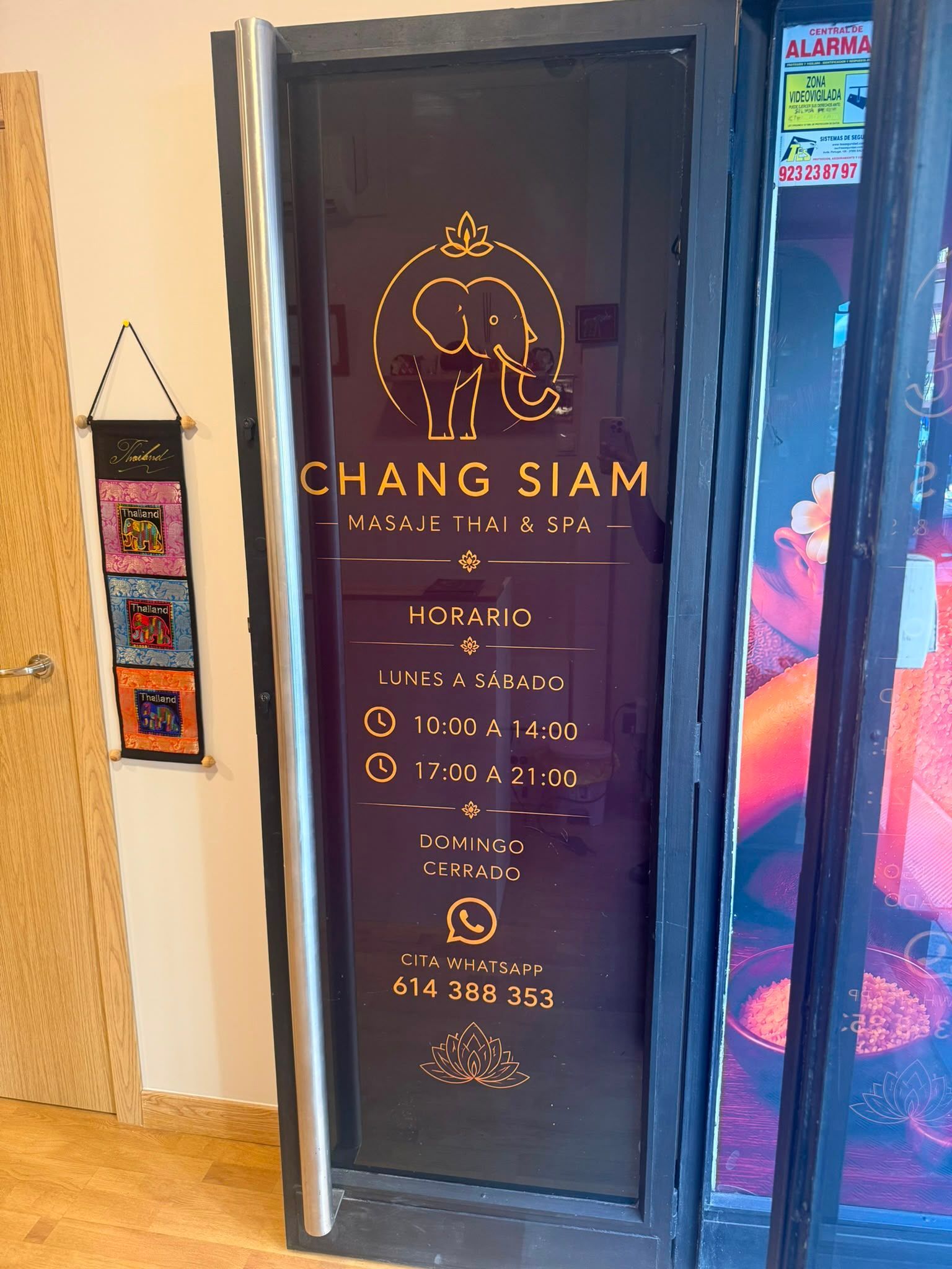 Puerta de color marrón oscuro del restaurante CHANG SIAM con logotipo y texto del menú en dorado, junto a coloridas obras de arte en la pared.