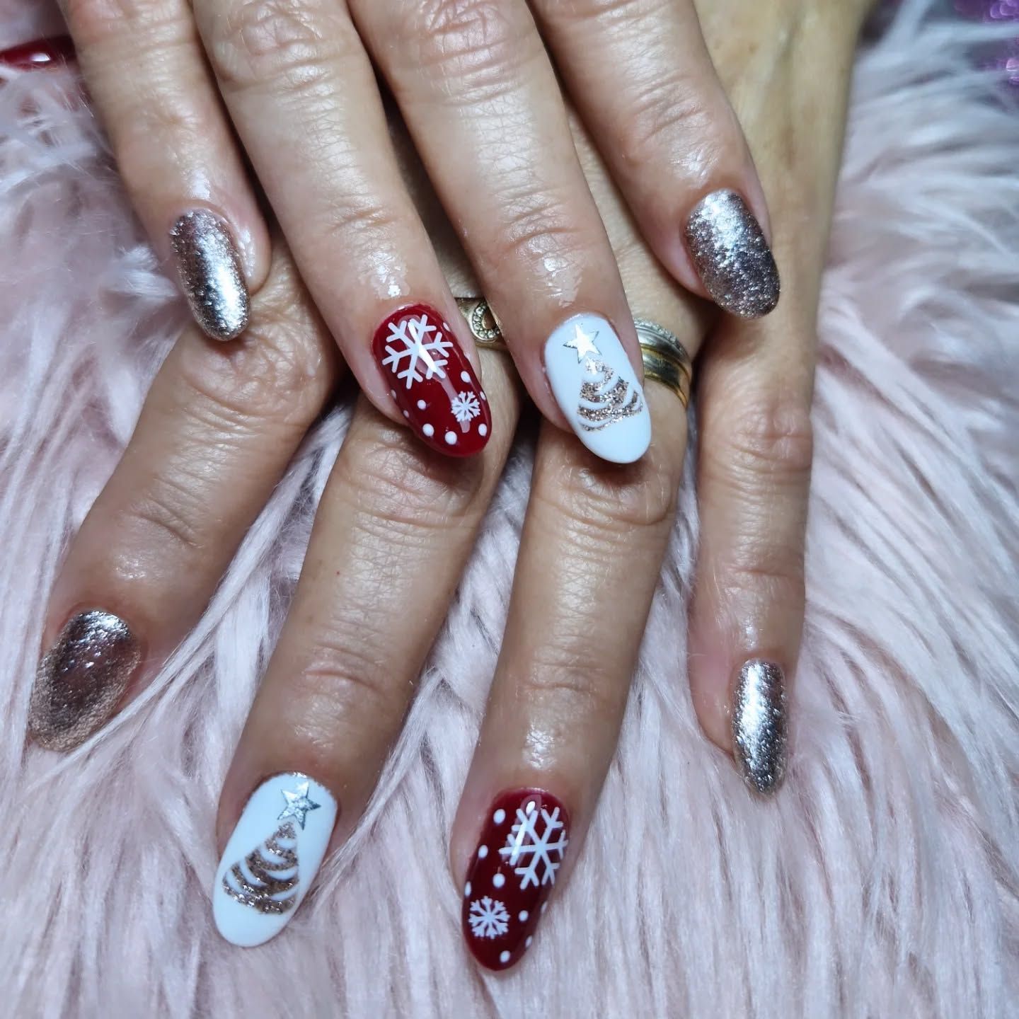 Manos con uñas decoradas con copos de nieve en tonos plateados metalizados, rojos y blancos sobre un fondo de pelo rosa suave