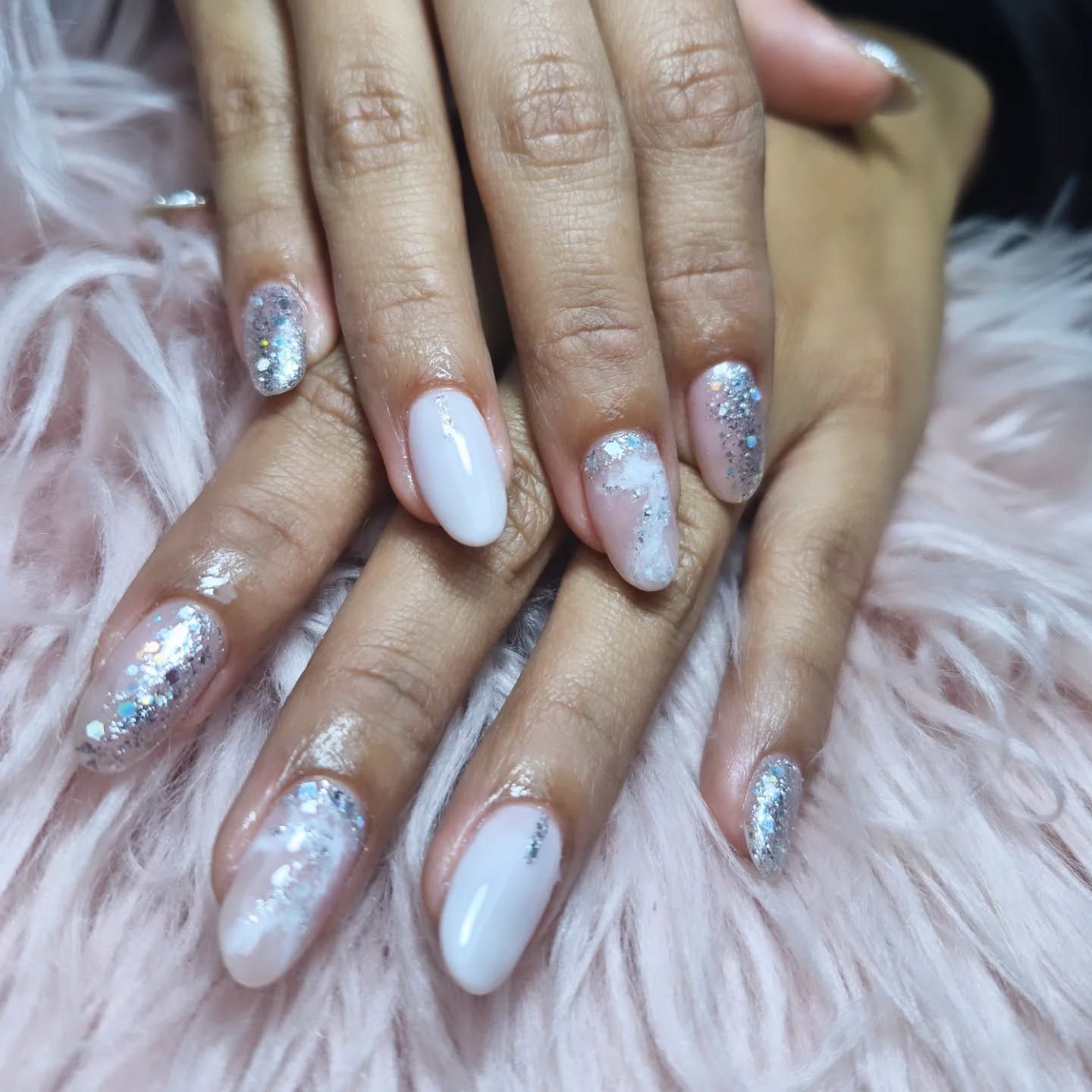 Manos con manicura larga blanca y con purpurina plateada sobre un fondo rosa suave y esponjoso