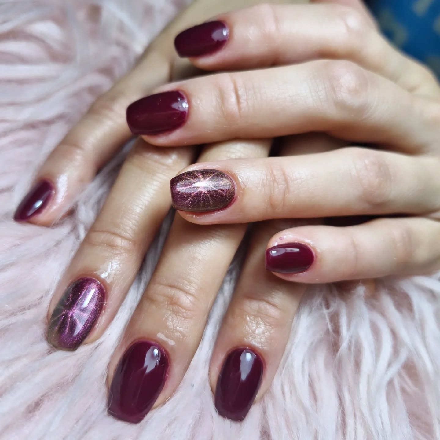 Manos con esmalte de uñas burdeos y con purpurina sobre un fondo rosa suave y peludo
