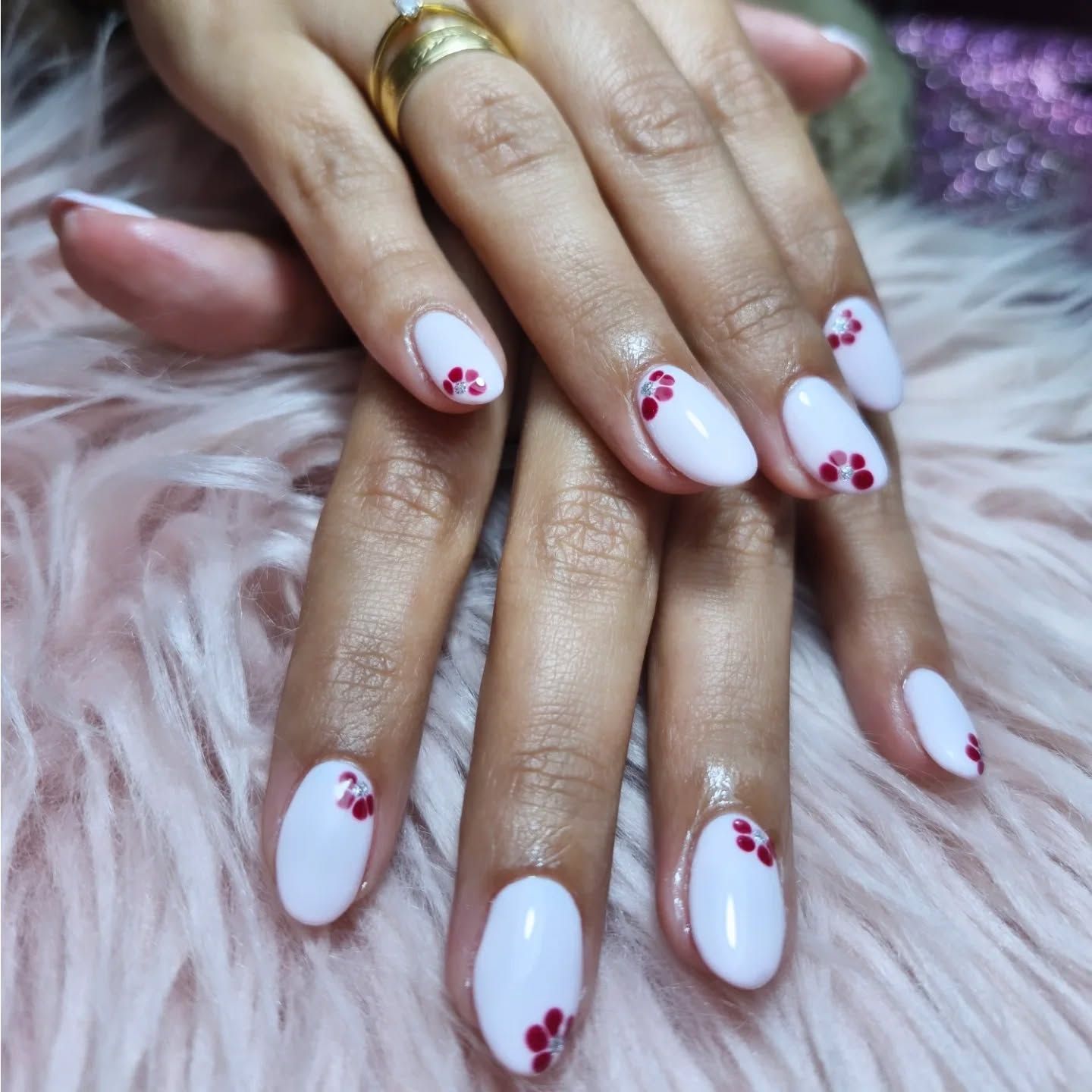 Manos con uñas blancas y detalles florales rojos sobre un fondo rosa de pelo largo
