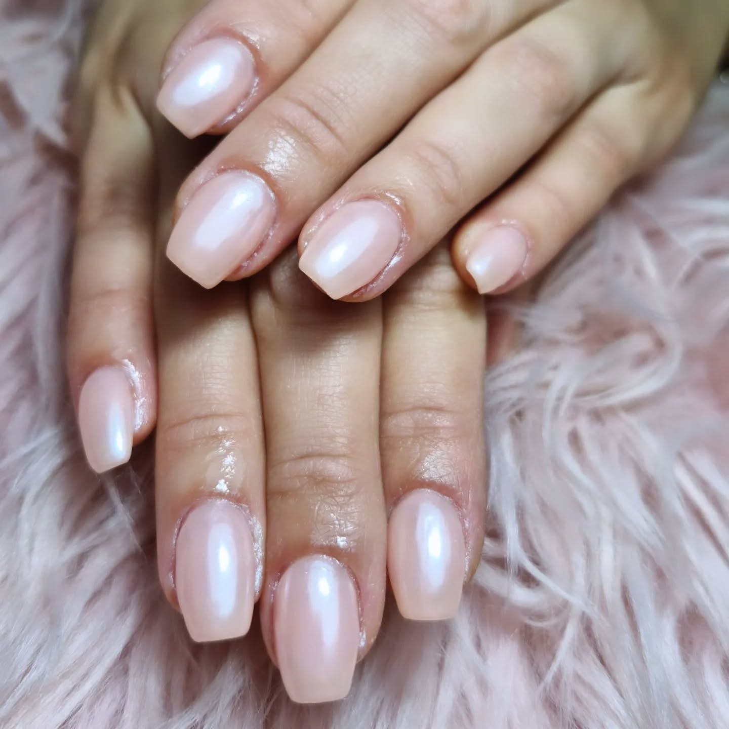 Manos cuidadas con uñas de color rosa pálido brillante apoyadas sobre una tela rosa suave con textura