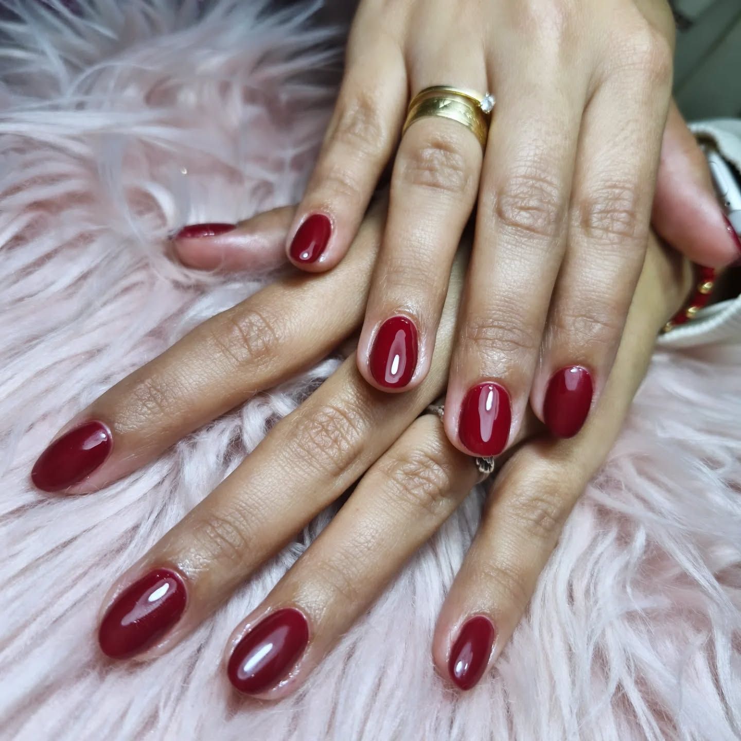 Manos con una manicura burdeos brillante apoyadas sobre pelo sintético rosa.