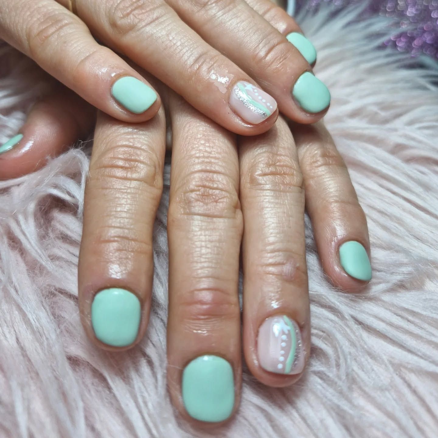 Manos con manicura verde menta sobre un fondo esponjoso rosa y morado