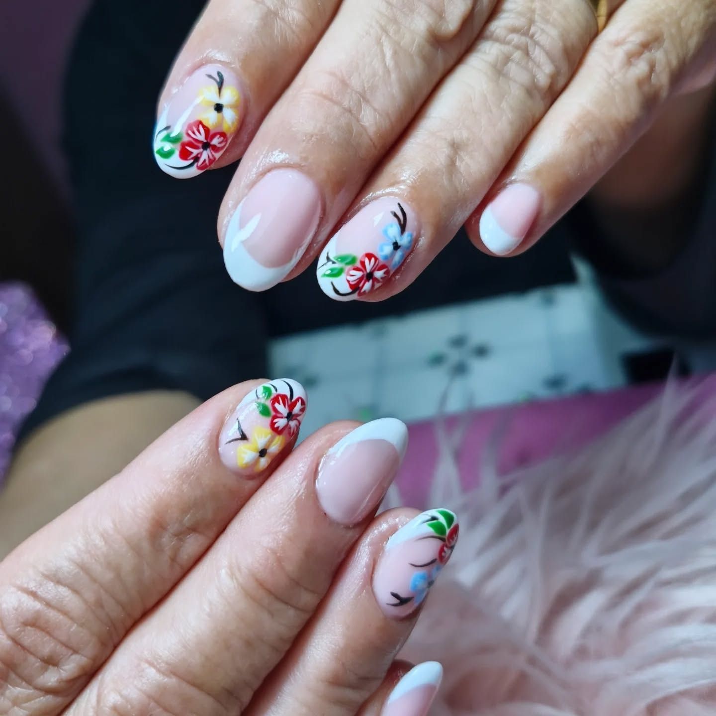 Manos con uñas rosa pastel y coloridos diseños florales sobre un fondo rosa suave y aterciopelado