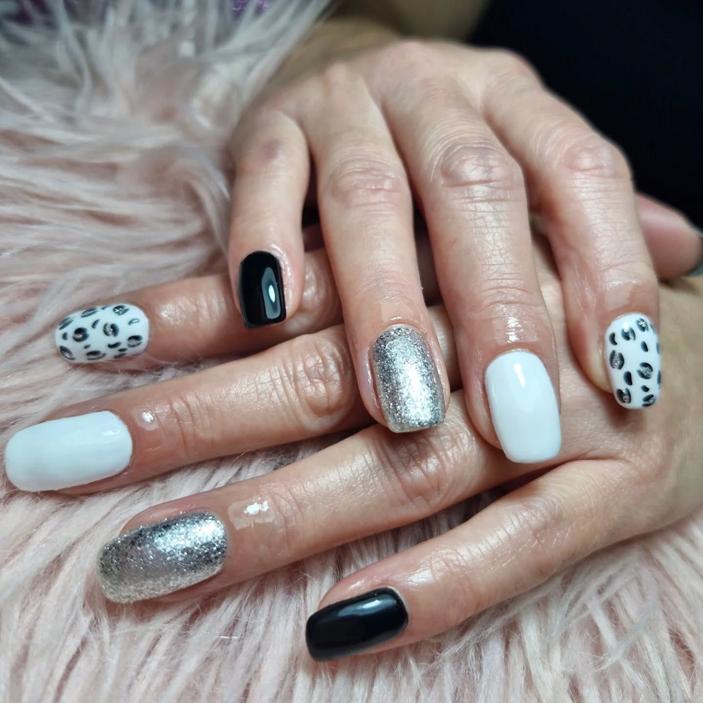 Primer plano de unas manos con las uñas arregladas y decoradas en negro, blanco y plateado, sobre un fondo rosa 