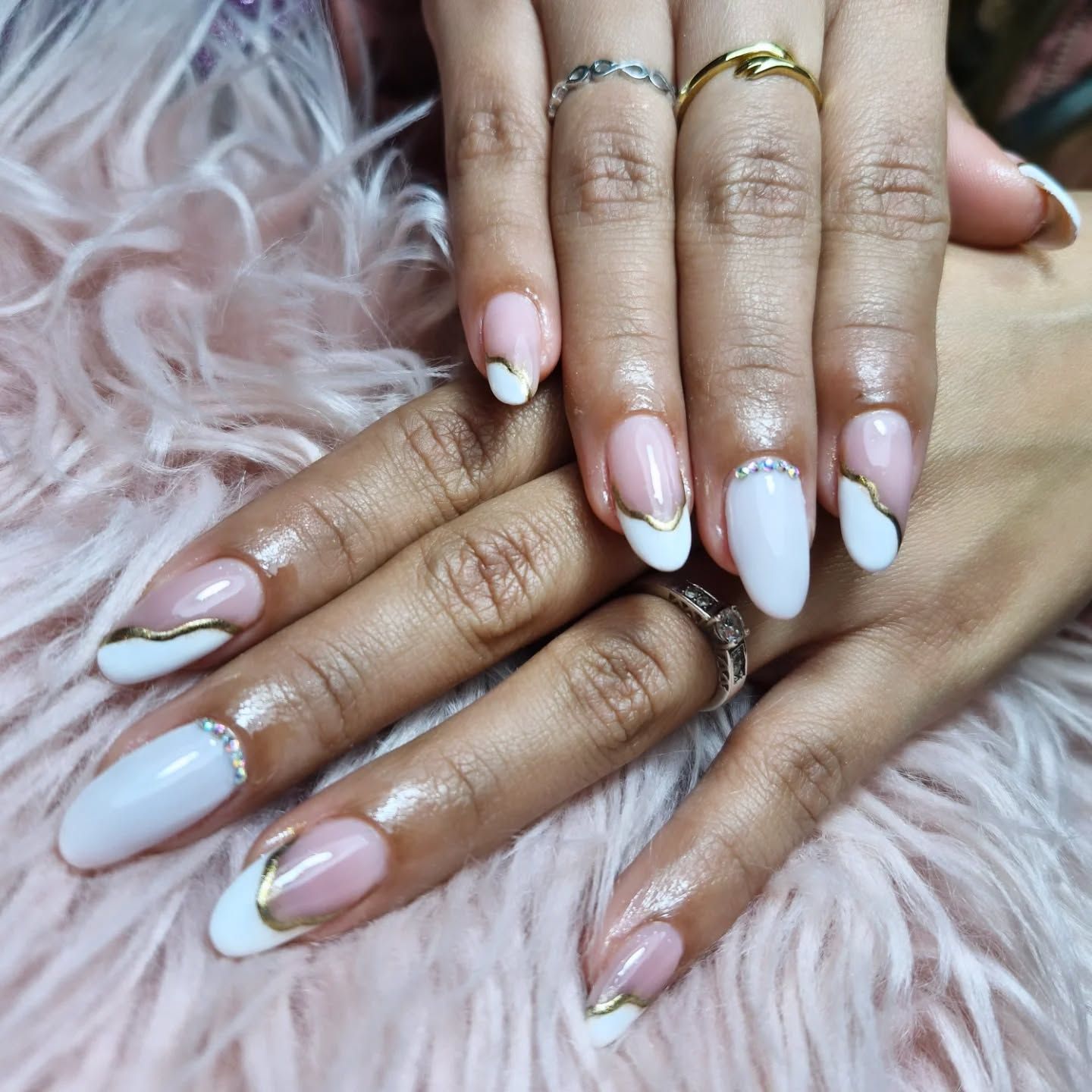 Manos con uñas largas cuidadas en tonos rosa pálido y blanco, apoyadas sobre una suave piel sintética rosa.