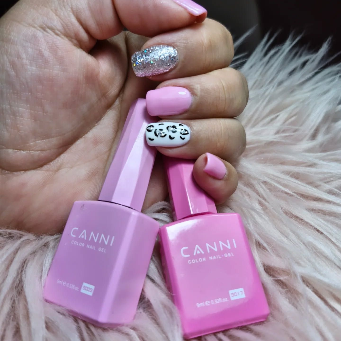 Una mano sostiene dos frascos rosas de esmalte de uñas CANNI, con unas uñas cuidadas al fondo