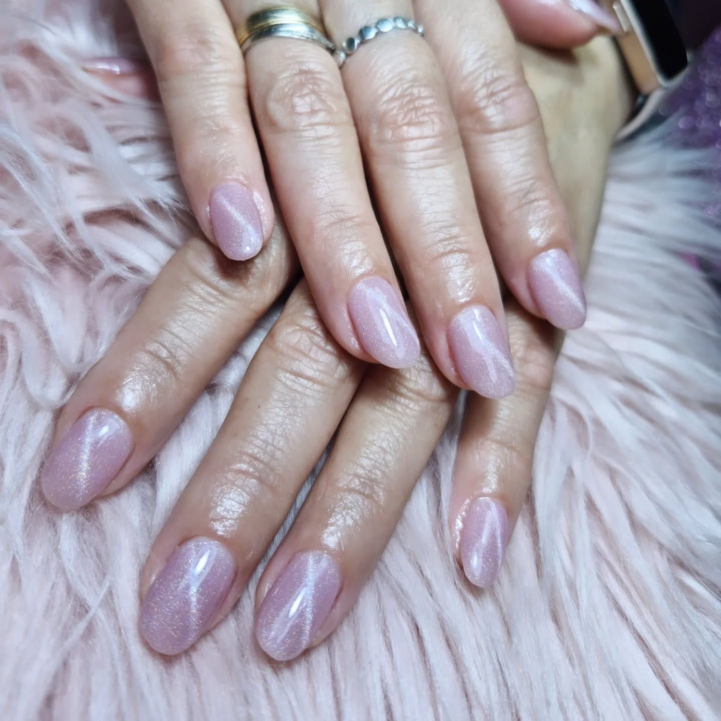 Manos con uñas cuidadas de color rosa pálido brillante apoyadas sobre una superficie rosa y mullida.