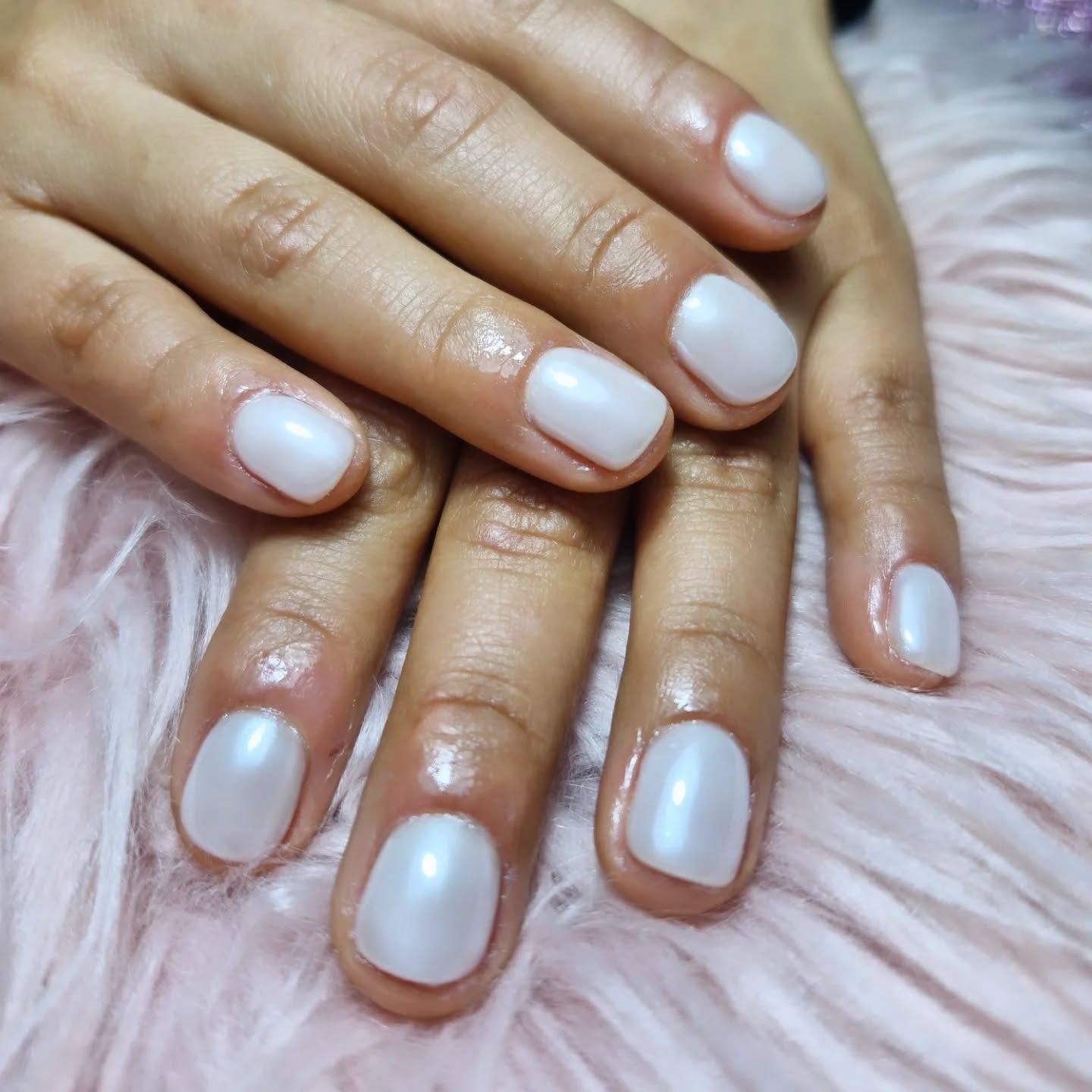 Manos con uñas arregladas de color rosa pálido sobre una superficie rosa suave y peluda