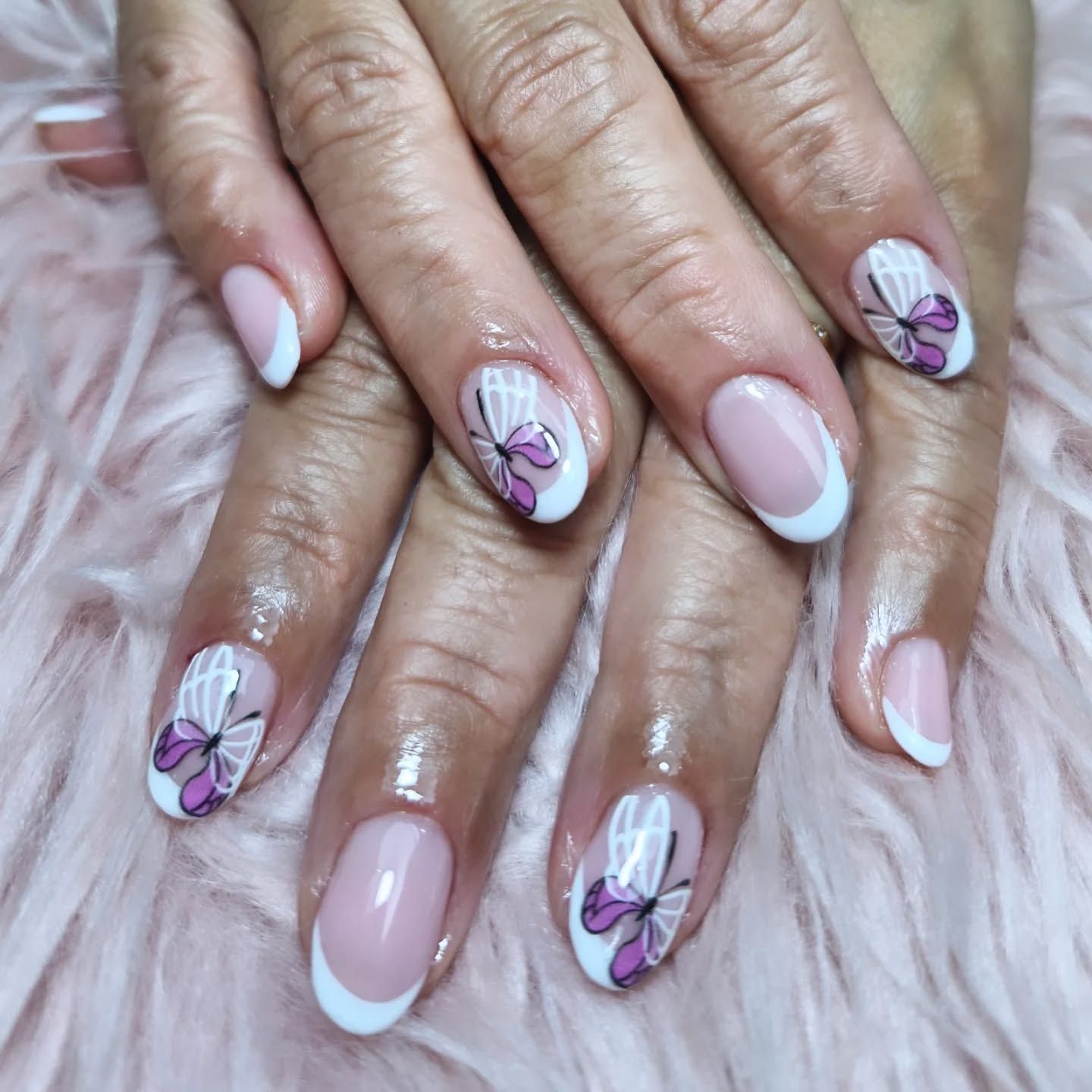 Manos con uñas decoradas con mariposas rosas y blancas brillantes