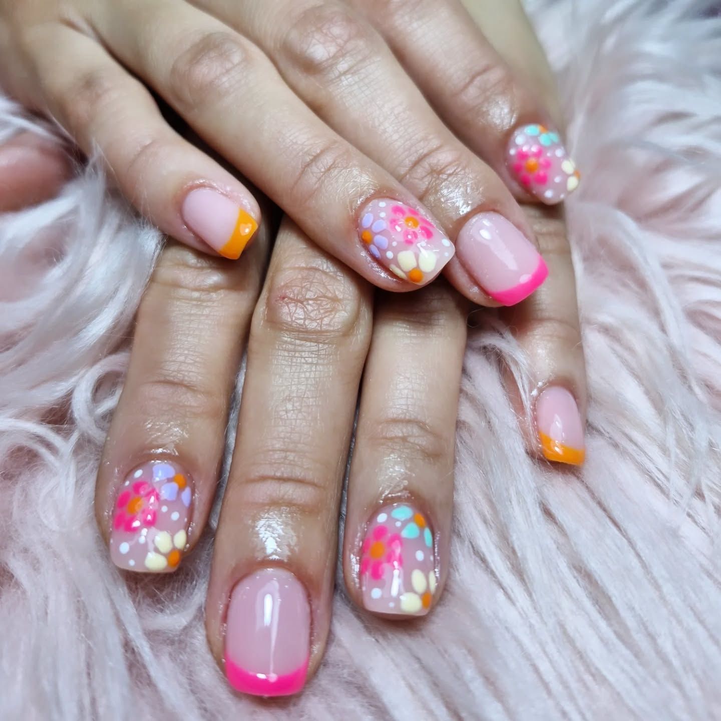 Manos con uñas decoradas en rosa pastel y detalles de confeti de colores sobre una tela blanca y esponjosa