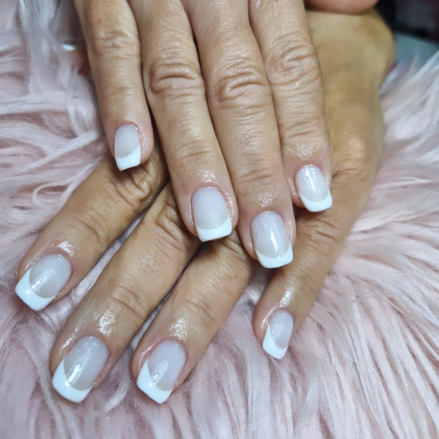 Manos con uñas blancas brillantes y cuidadas sobre una superficie suave y esponjosa de color rosa