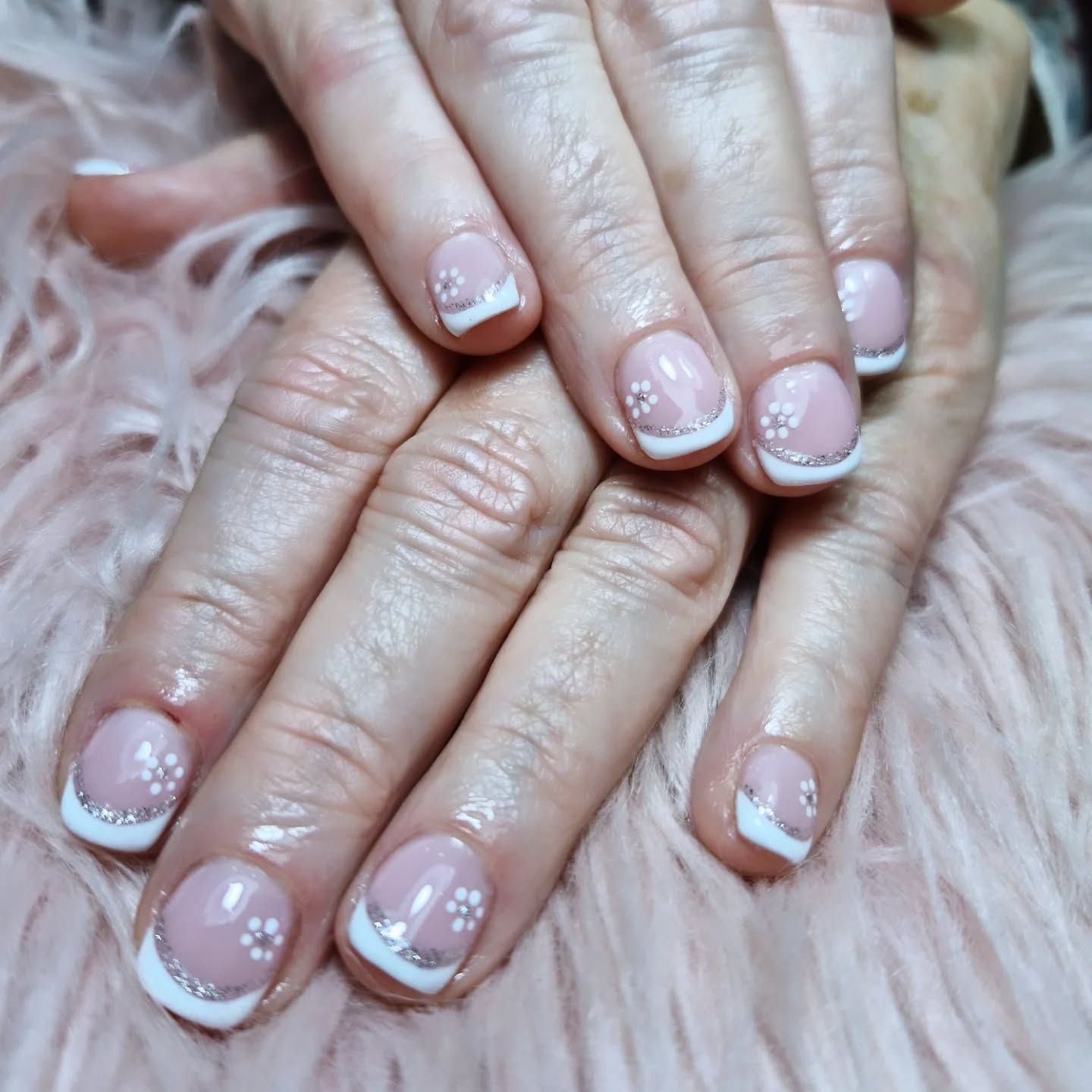 Manos con manicura francesa rosa pálido sobre una superficie rosa mullida