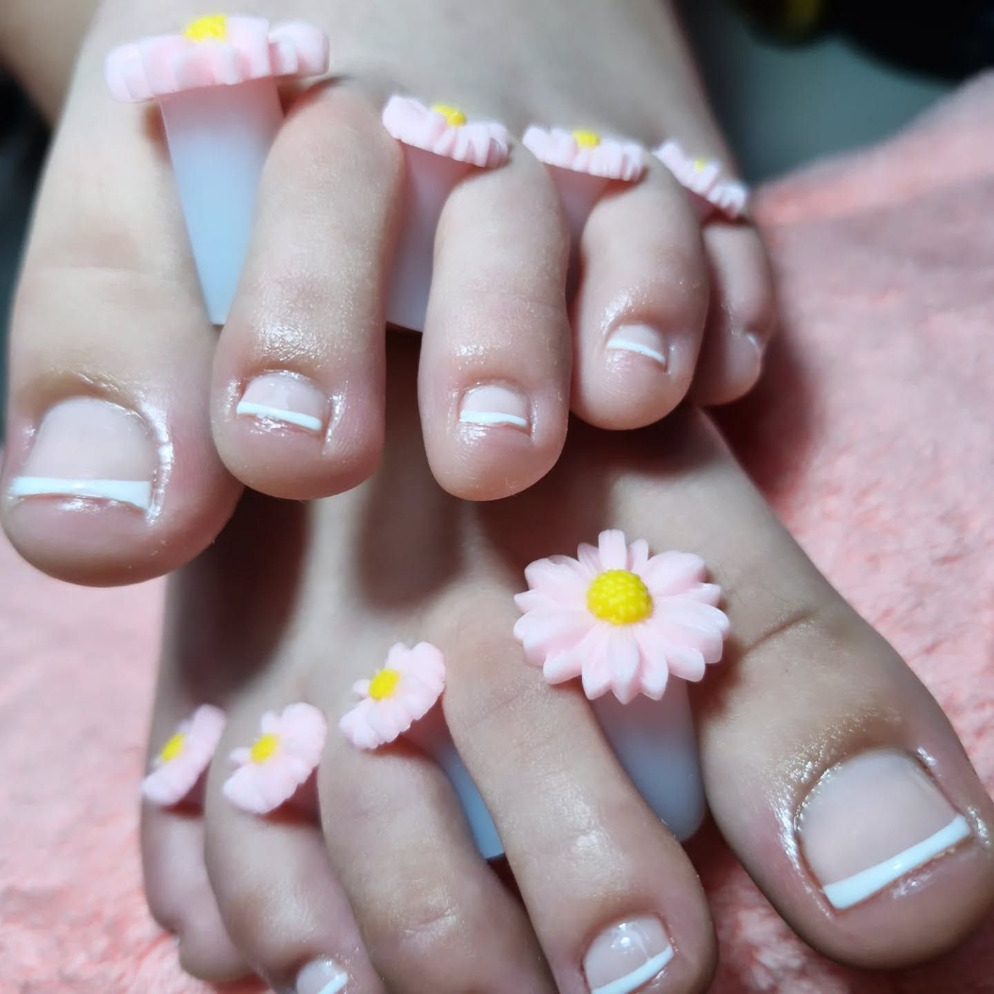 Uñas decoradas con pequeñas margaritas rosas y blancas sobre un fondo rosa suave
