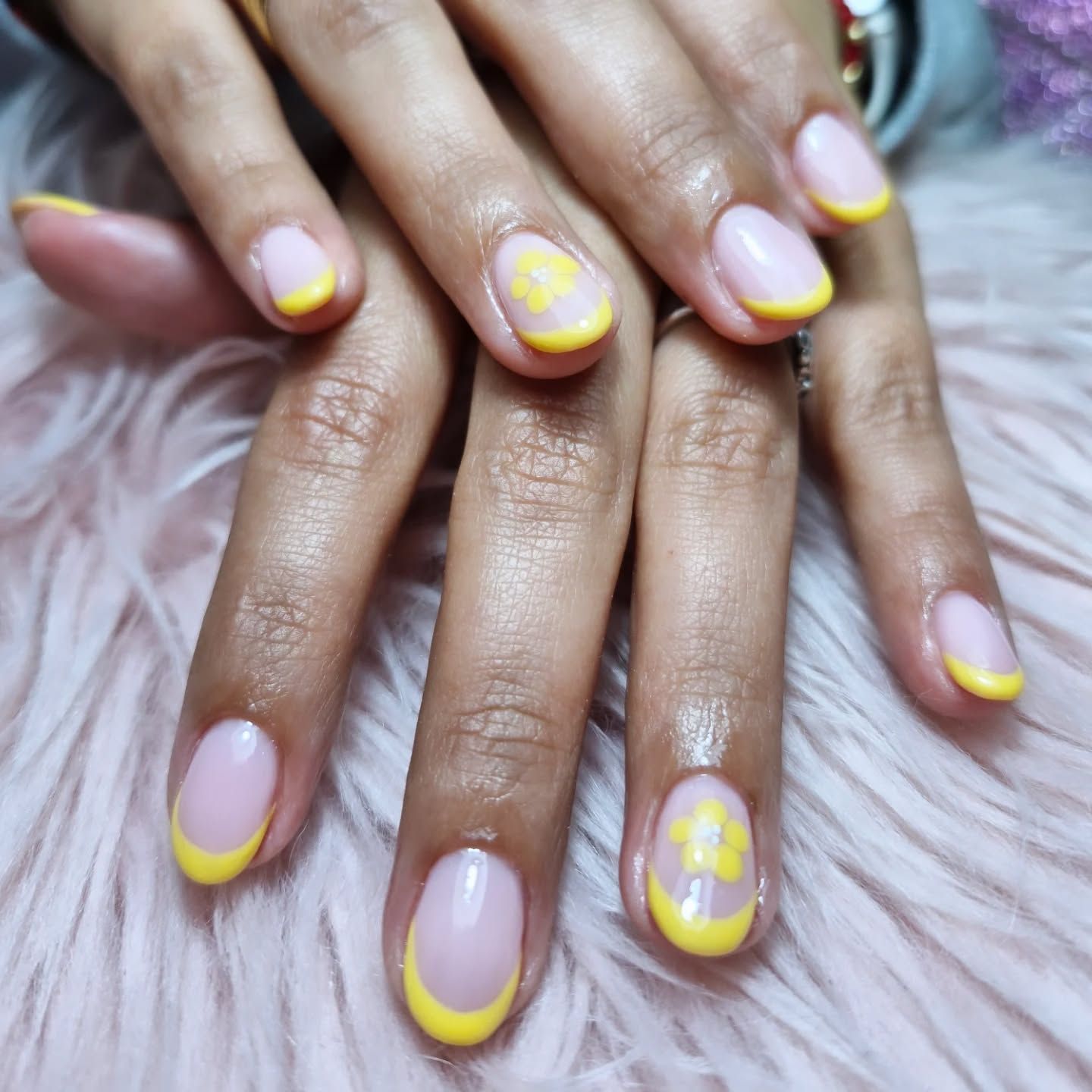 Manos con manicura en tonos nude y amarillo sobre una superficie rosa mullida