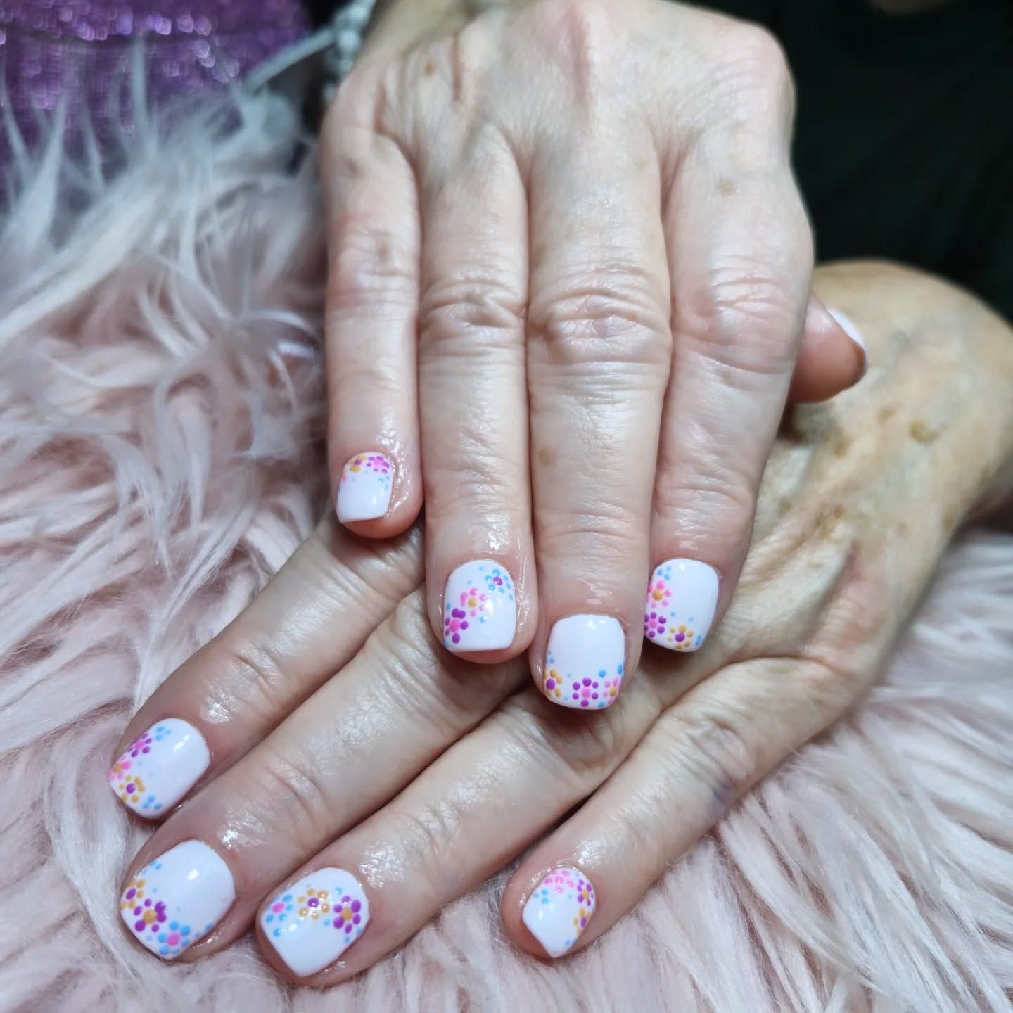 Manos con las uñas pintadas de blanco y purpurina rosa sobre un pelaje suave.