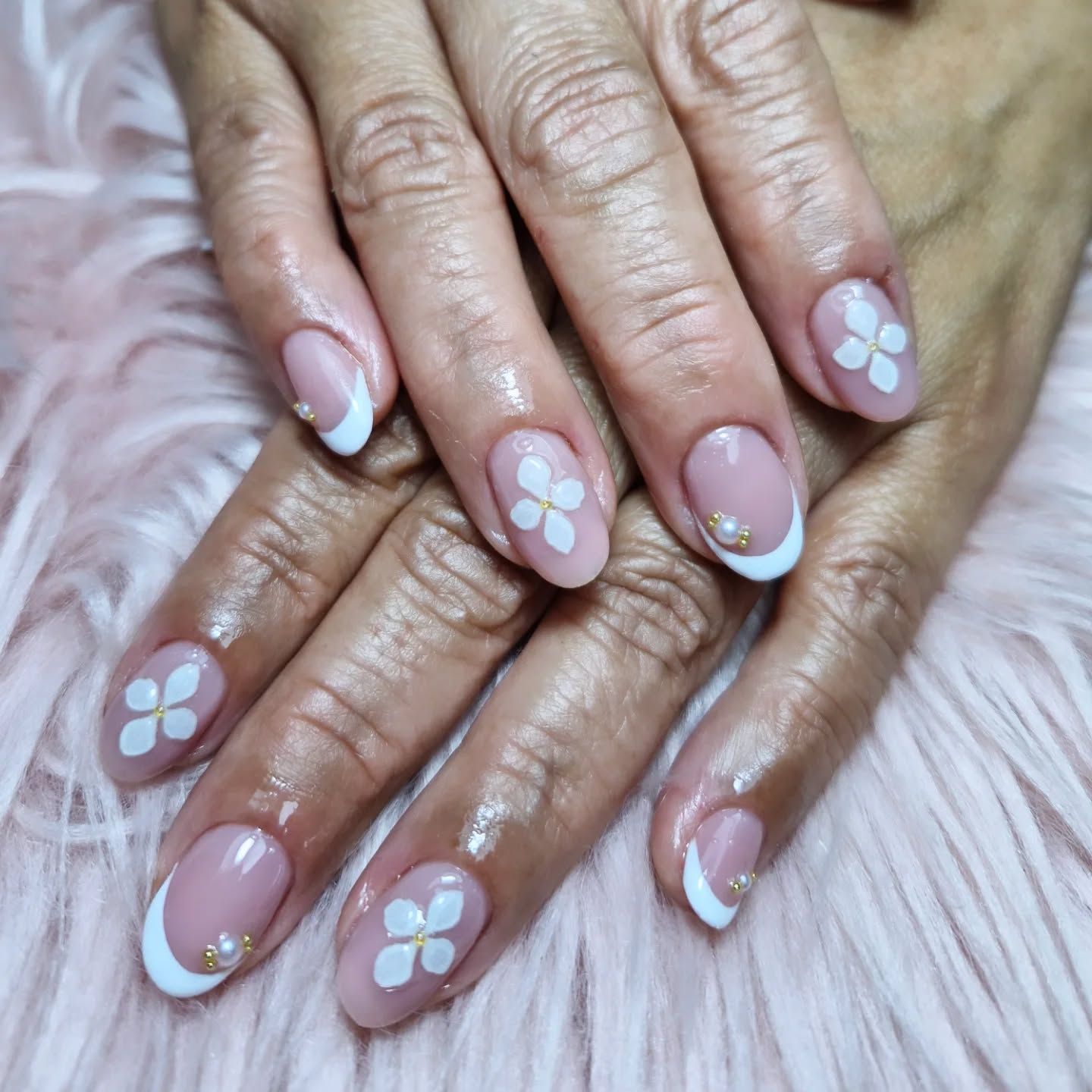 Primer plano de unas manos con uñas decoradas con flores rosa pálido y puntas francesas blancas sobre un fondo suave 