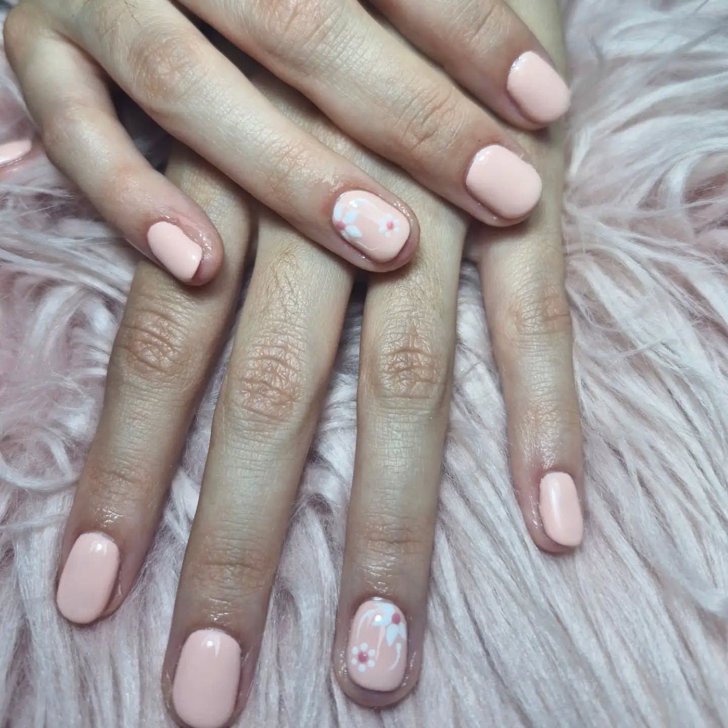 Manos con uñas cuidadas de color rosa pálido sobre un fondo de pelo rosa suave.
