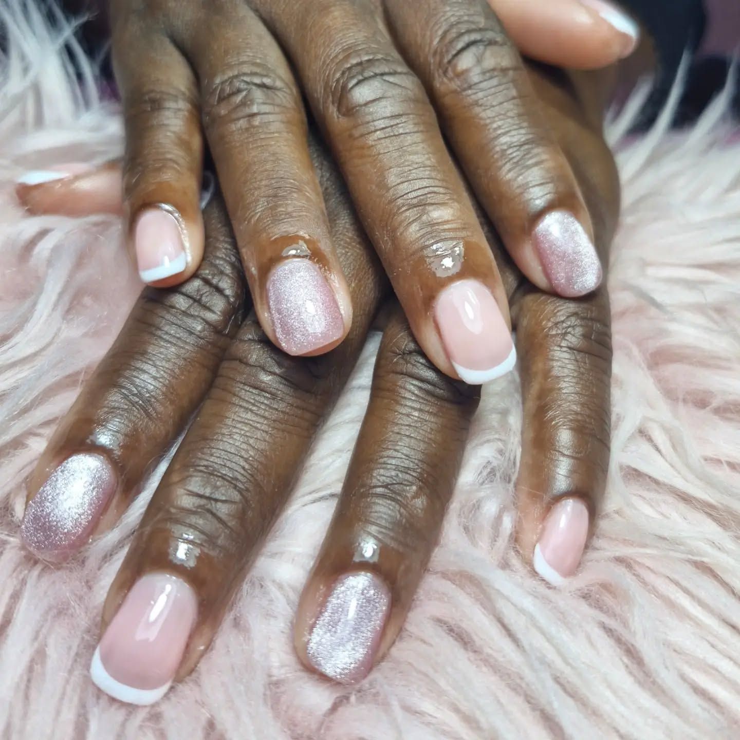 Manos con manicura de purpurina rosa claro apoyadas sobre una superficie blanca y mullida