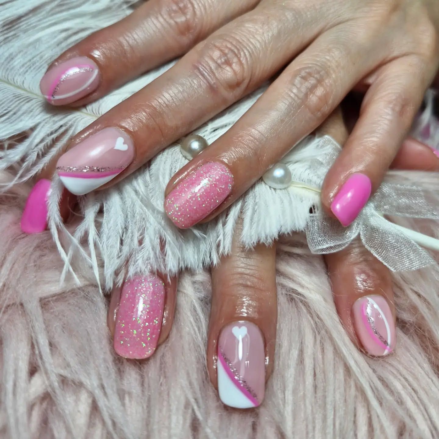 Manicura rosa con purpurina y corazones en uñas largas, sobre un suave fondo blanco de pelo sintético