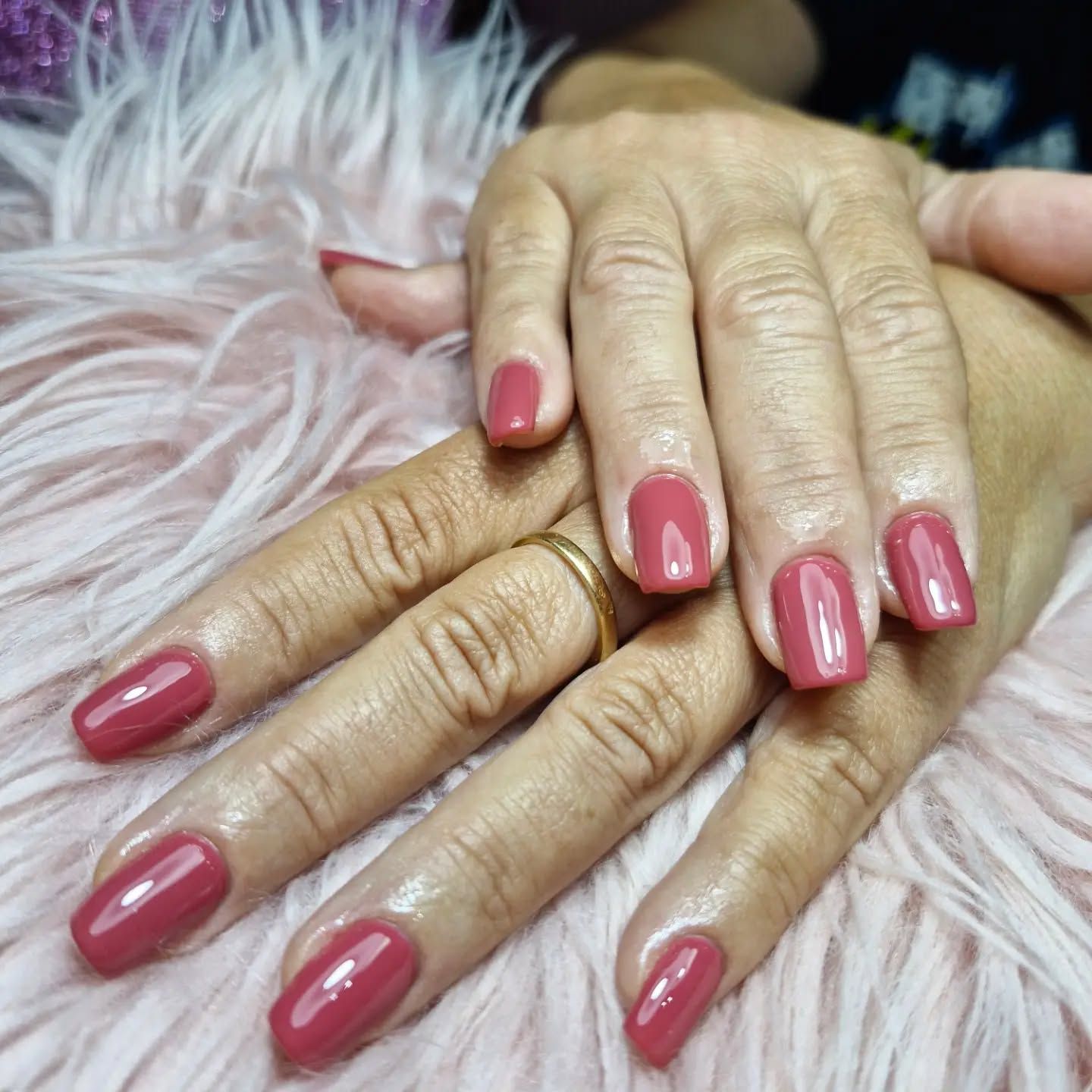 Dos manos con las uñas arregladas en rosa brillante sobre una suave piel rosa.