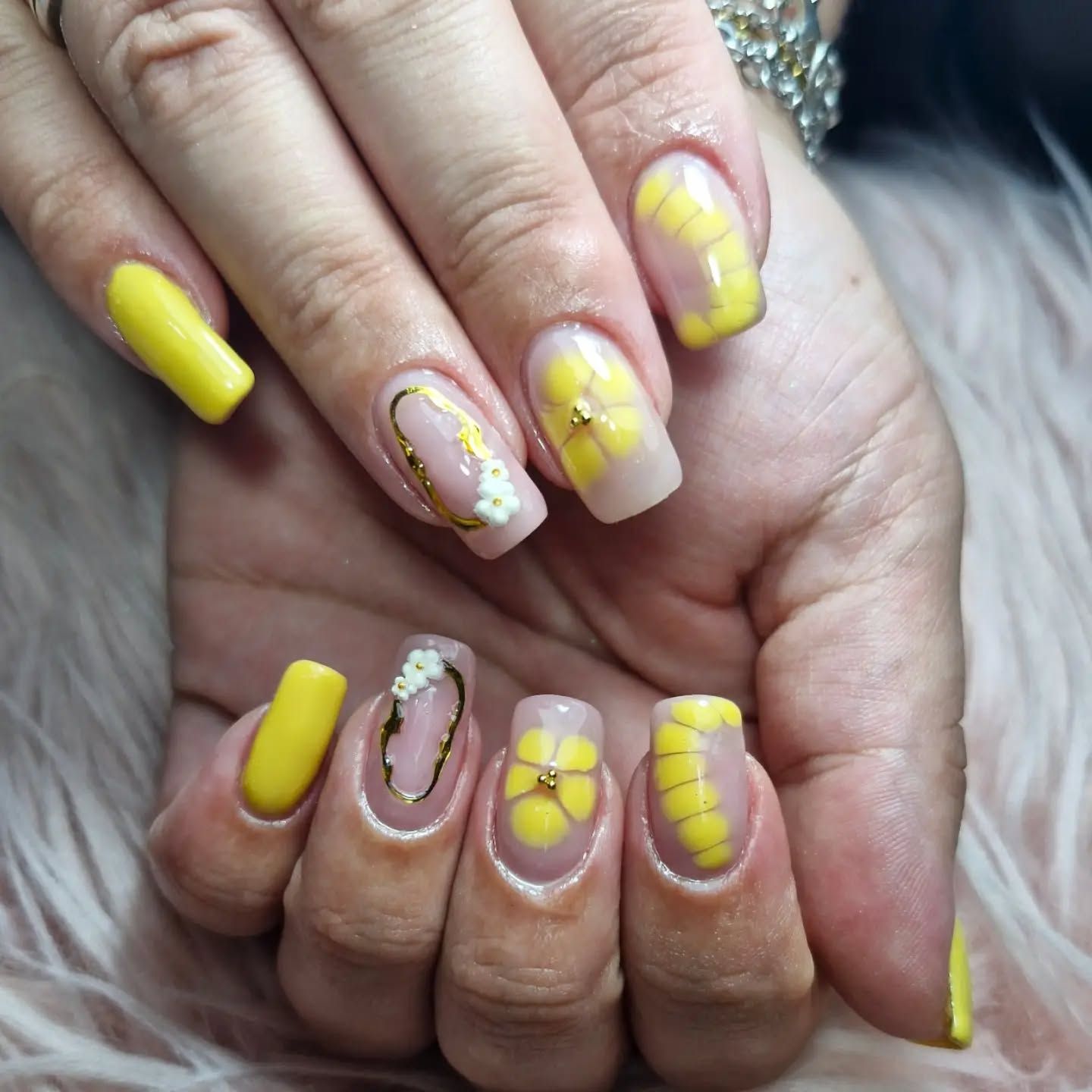 Manos con uñas amarillas cuidadosamente pintadas y motivos florales blancos, juntas en primer plano.