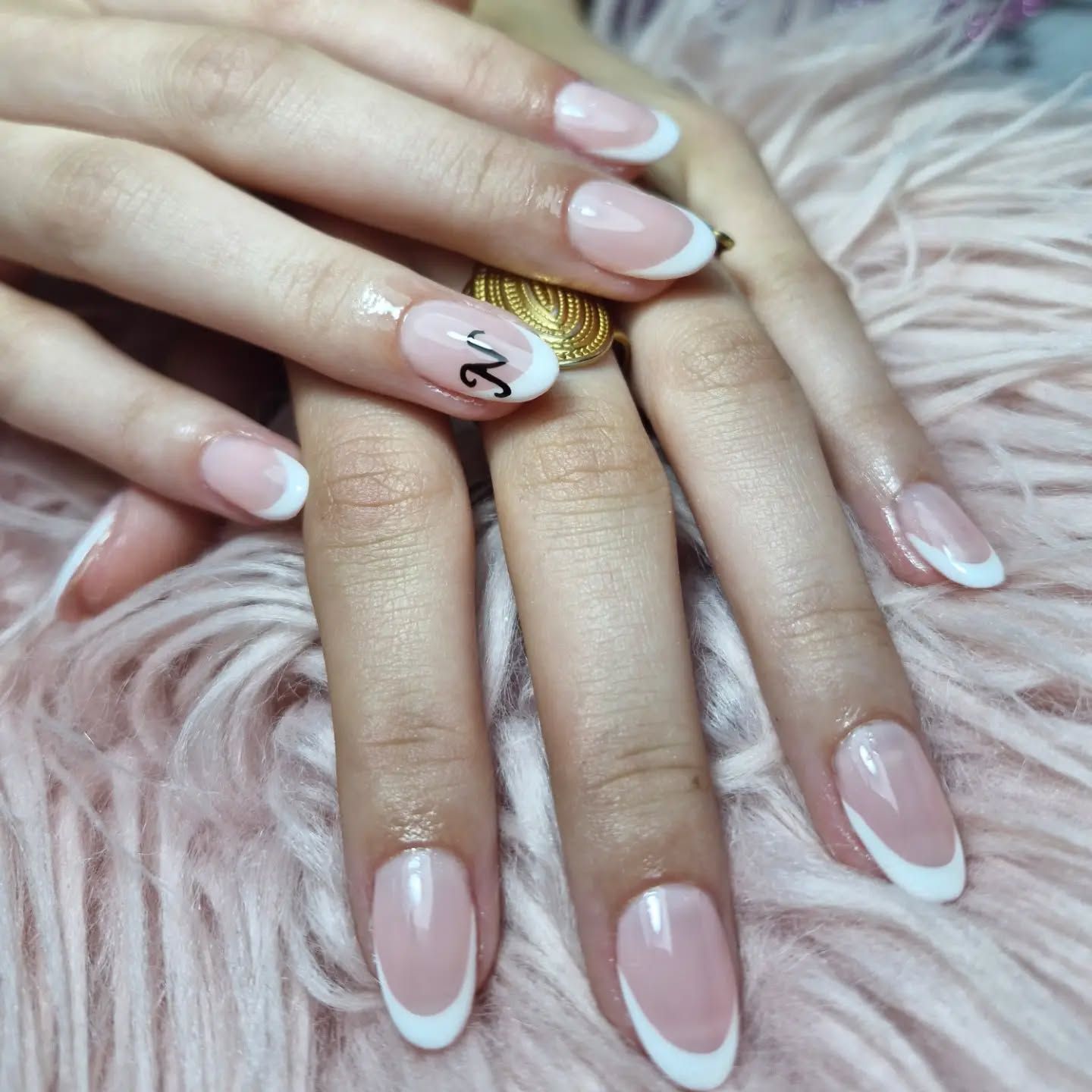 Manos con manicura francesa rosa pálido descansando sobre un suave pelaje rosa y luciendo un anillo de oro.