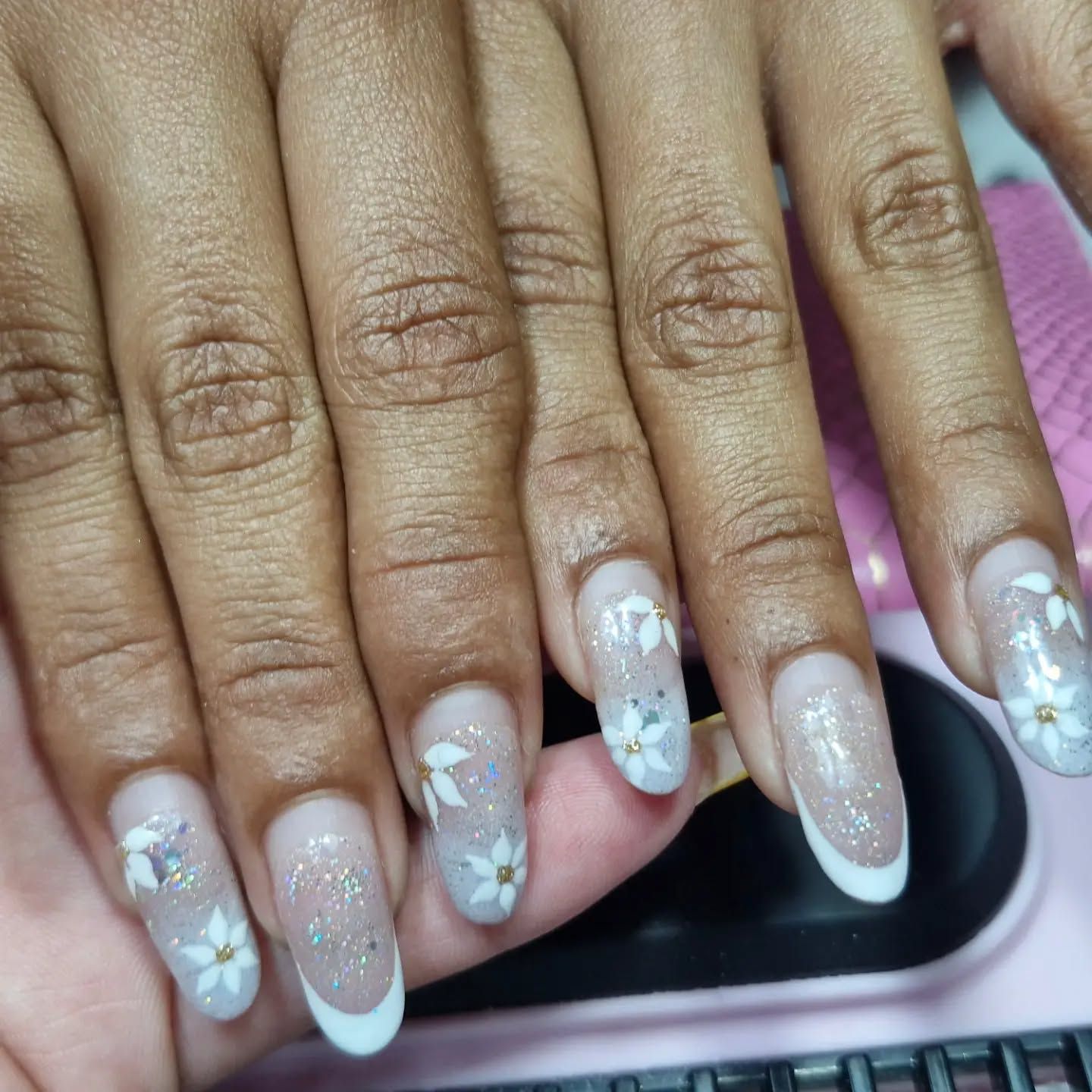 Mano con uñas largas decoradas con flores blancas y manicura con degradado brillante sobre un fondo rosa