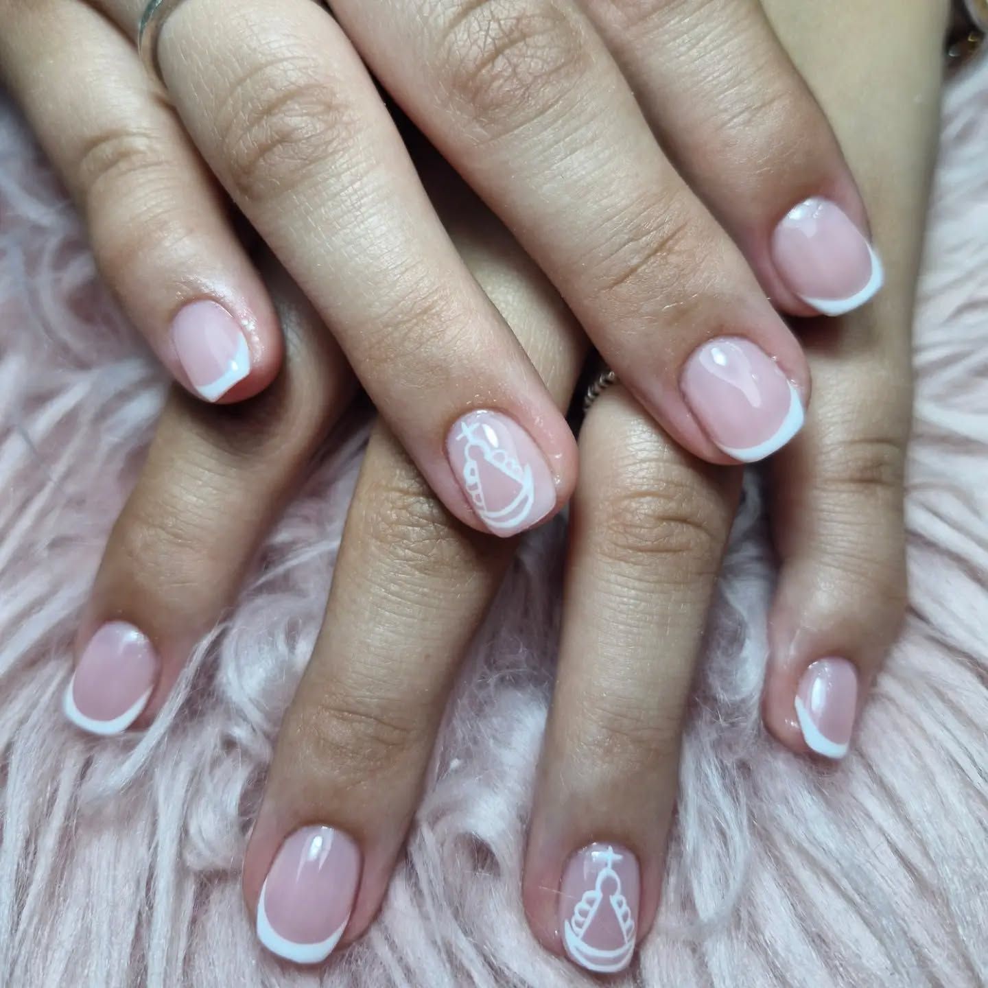 Primer plano de unas manos con manicura francesa en rosa pálido y decoración blanca en las uñas.