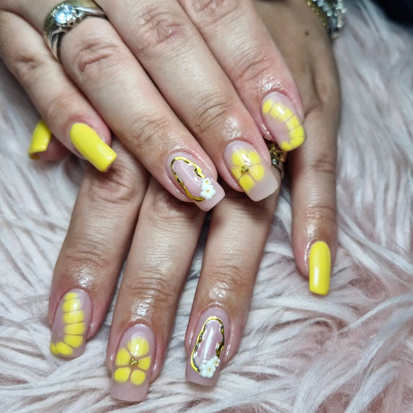 Manos con uñas decoradas de color amarillo brillante sobre un fondo rosa suave y afelpado