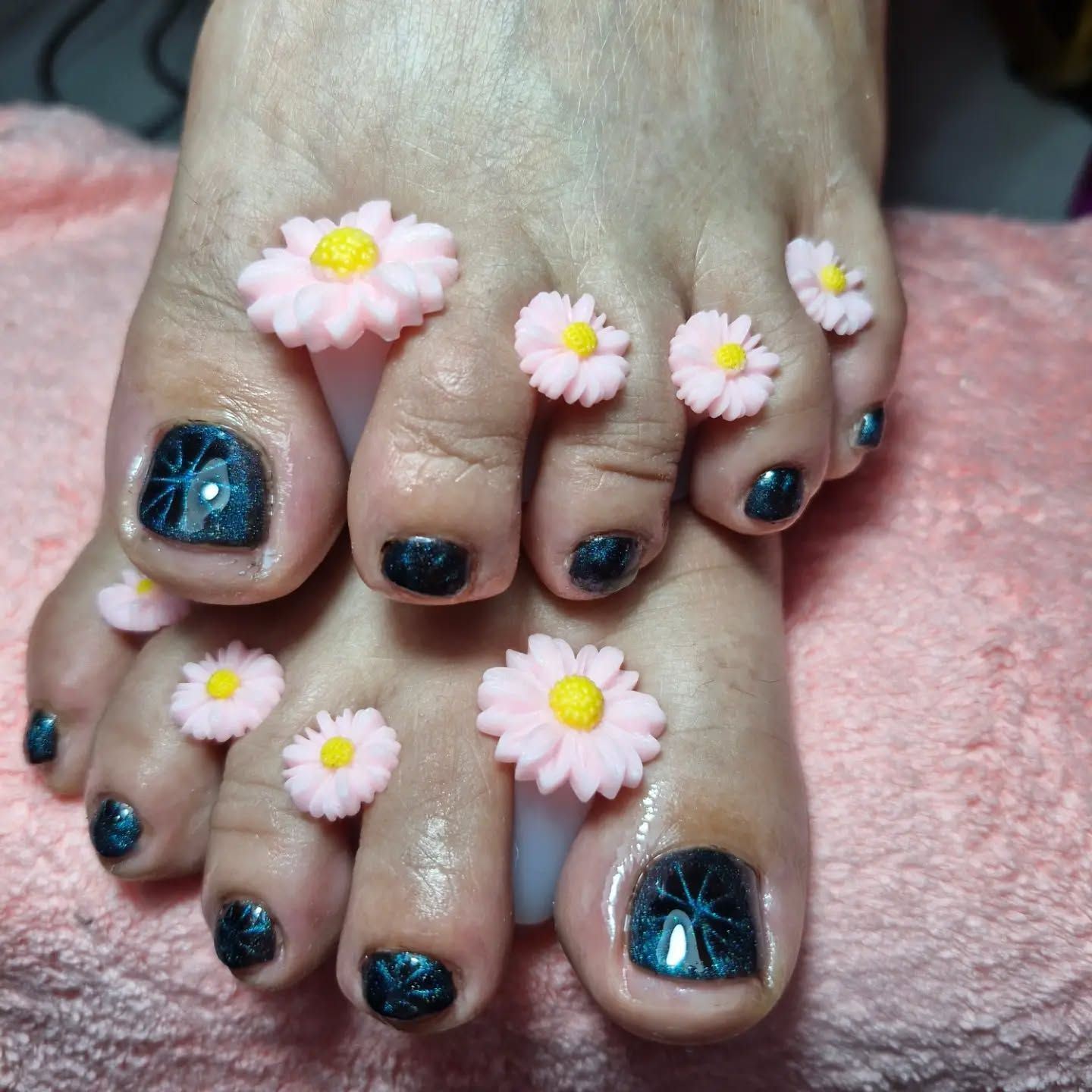 Dedos de los pies con esmalte verde azulado oscuro y margaritas decoradas en las uñas, sobre una manta rosa suave