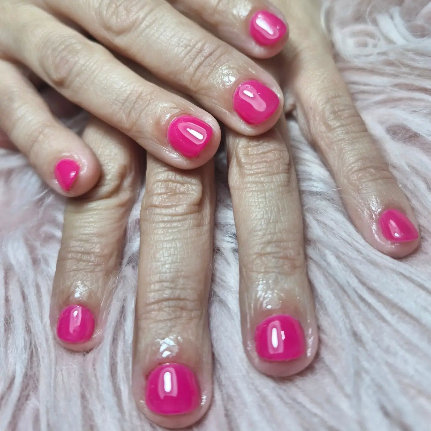 Primer plano de unas manos con las uñas pintadas de rosa intenso apoyadas sobre una superficie blanca y suave