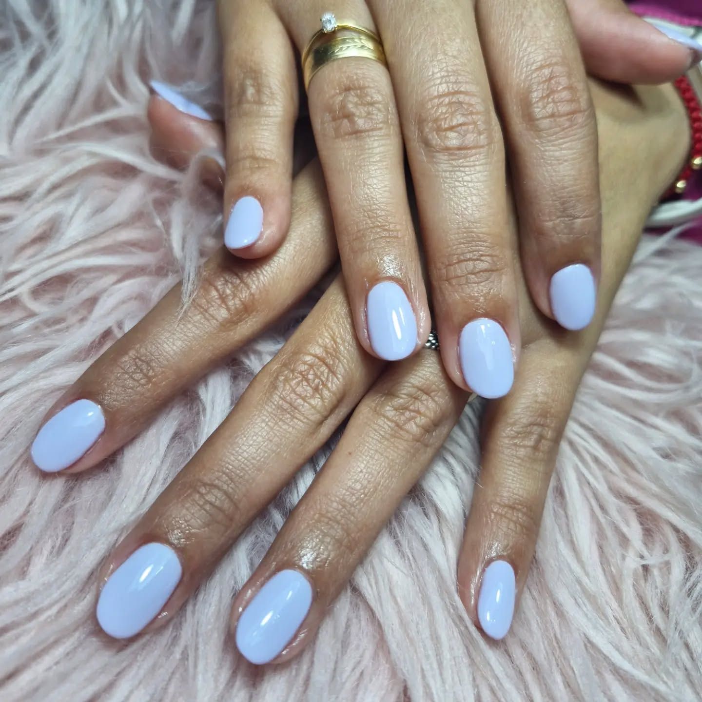 Manos con uñas pintadas de azul pastel apoyadas sobre una superficie rosa y esponjosa.