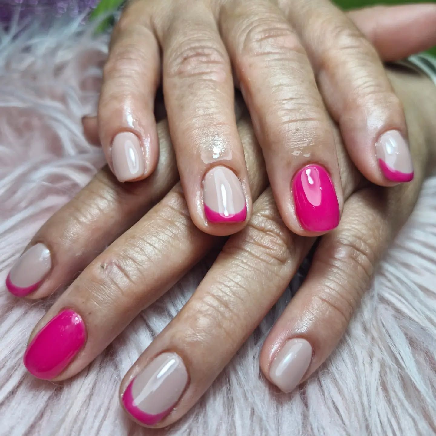 Manos con uñas cuidadas en tonos rosa brillante y nude, apoyadas juntas sobre una superficie mullida