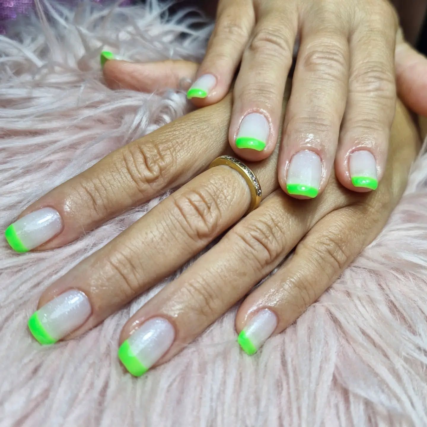 Manos con manicura francesa verde neón y anillos dorados sobre un fondo rosa de pelo largo