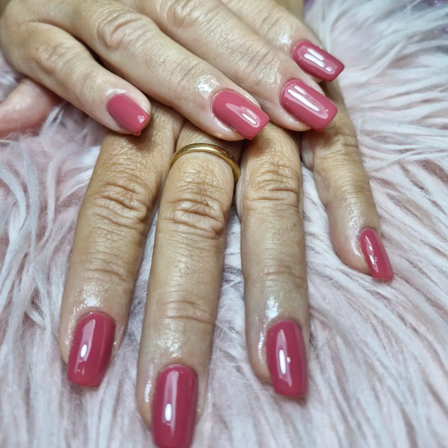 Manos con uñas manicuras de color rosa brillante sobre un fondo de pelo rosa suave