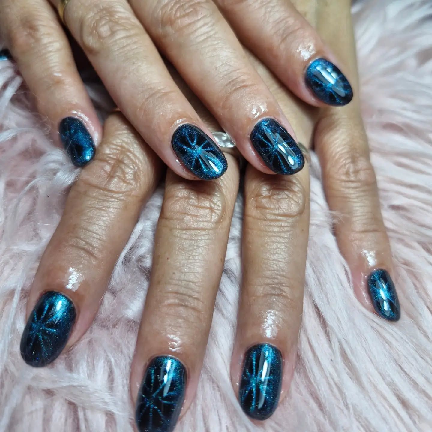 Manos con uñas decoradas con purpurina azul metálica sobre una superficie rosa mullida