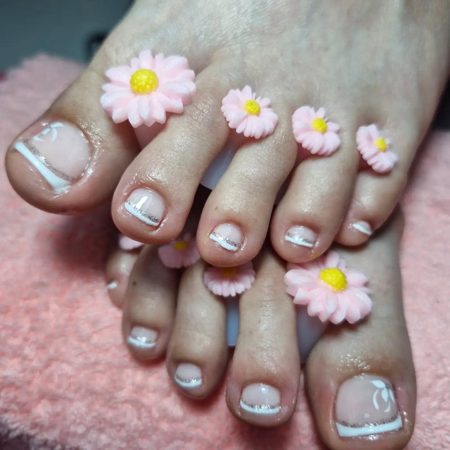 Uñas de los pies pintadas y anillos para los dedos con margaritas rosas, en unos pies cruzados