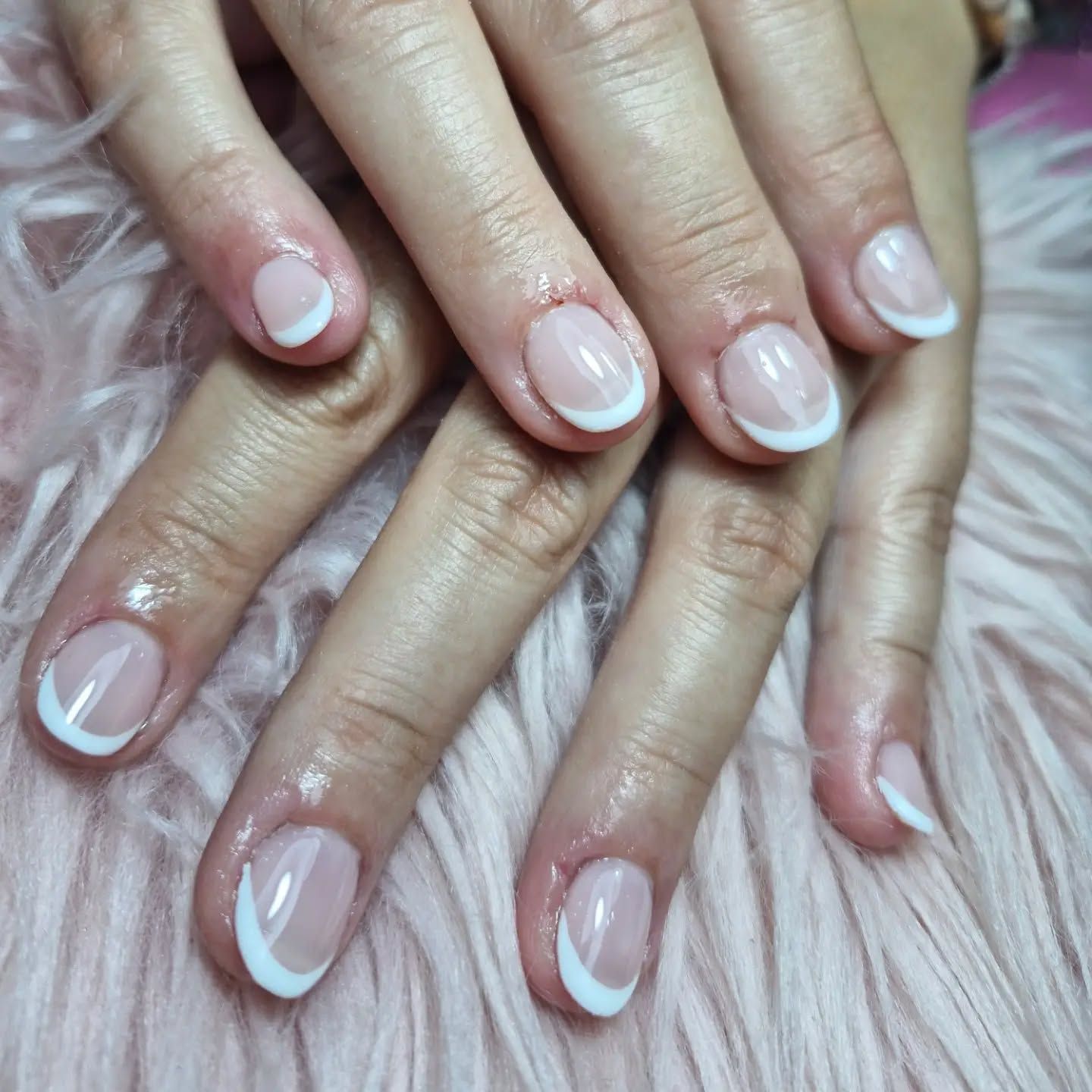 Manos cuidadas con uñas de color rosa pálido brillante sobre un fondo de suave pelaje rosa
