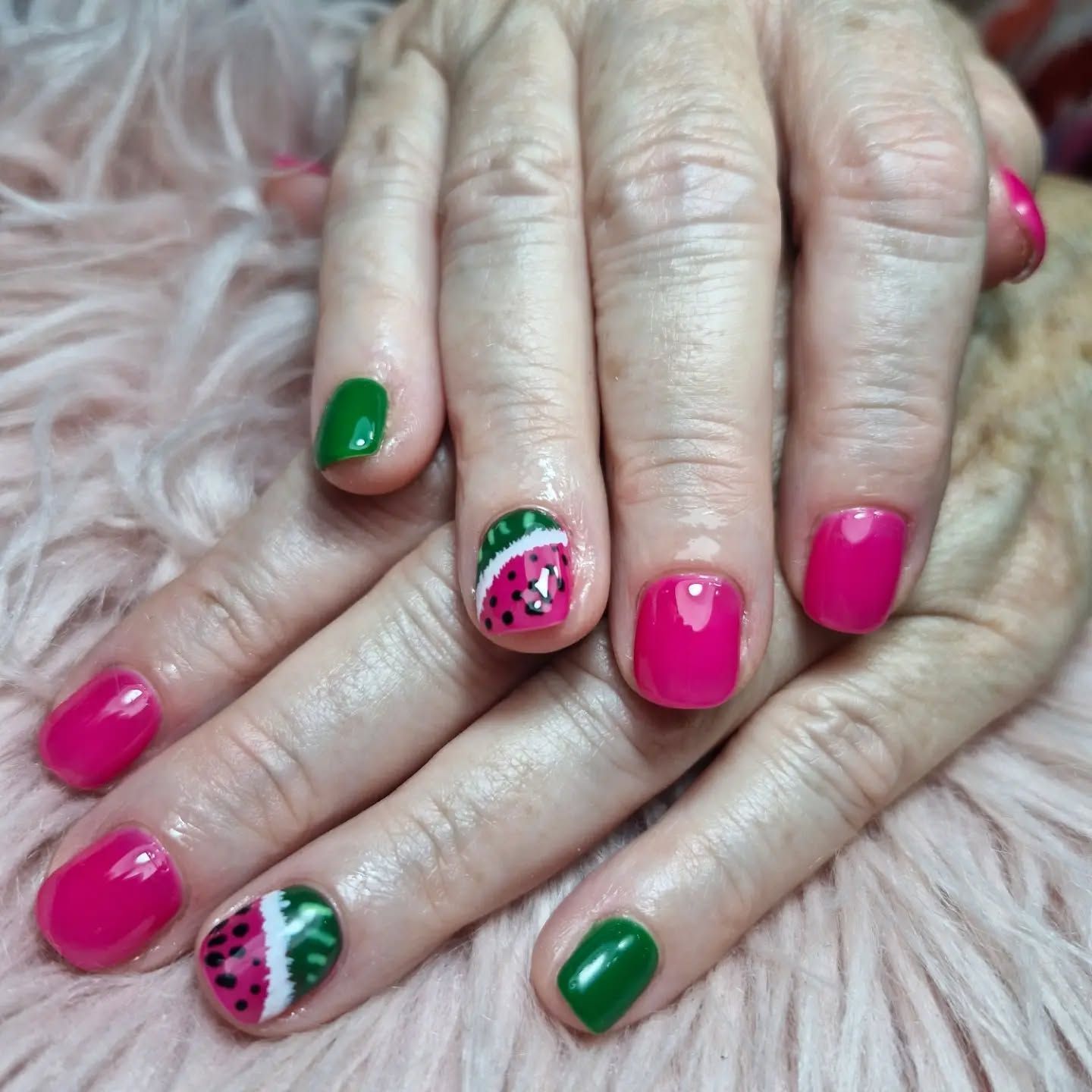 Manos con uñas cuidadas de color rosa intenso y verde, algunas con diseños de sandía.
