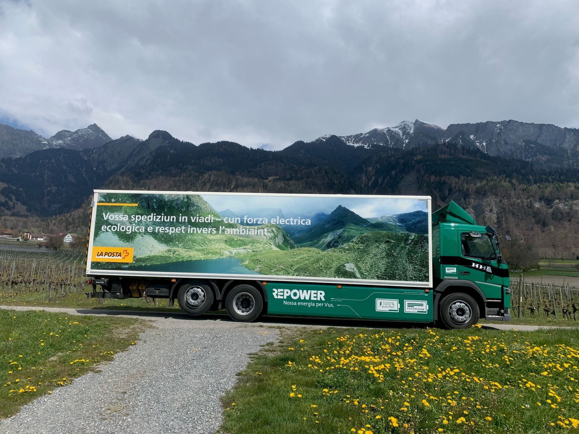 Ein grüner Lastwagen parkt auf einem Feld mit Bergen im Hintergrund.