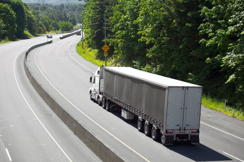Un camión semirremolque circula por una autopista junto a árboles.
