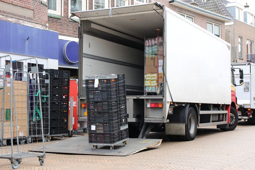 Dos camiones están estacionados frente a una tienda con las puertas traseras abiertas.