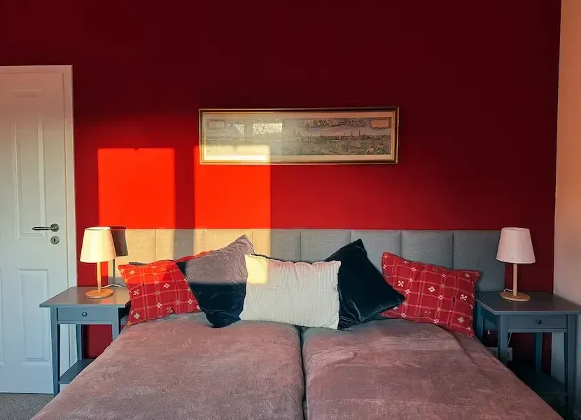 A bedroom with two beds and a red wall