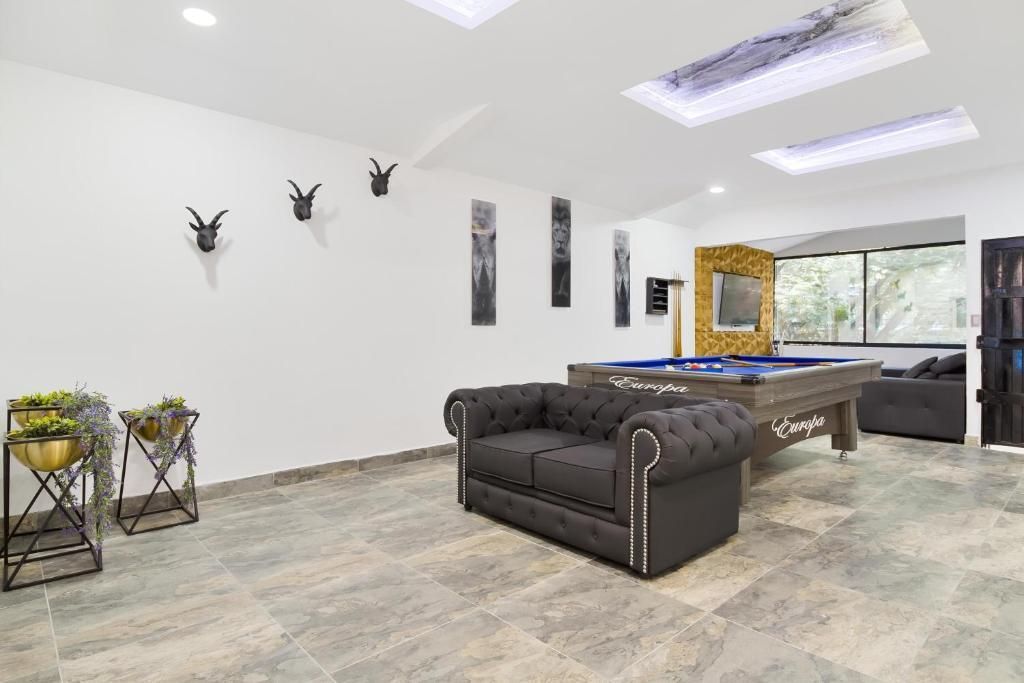 A game room with a grey tufted sofa, a pool table, tiled floors, skylights, and wall decorations.