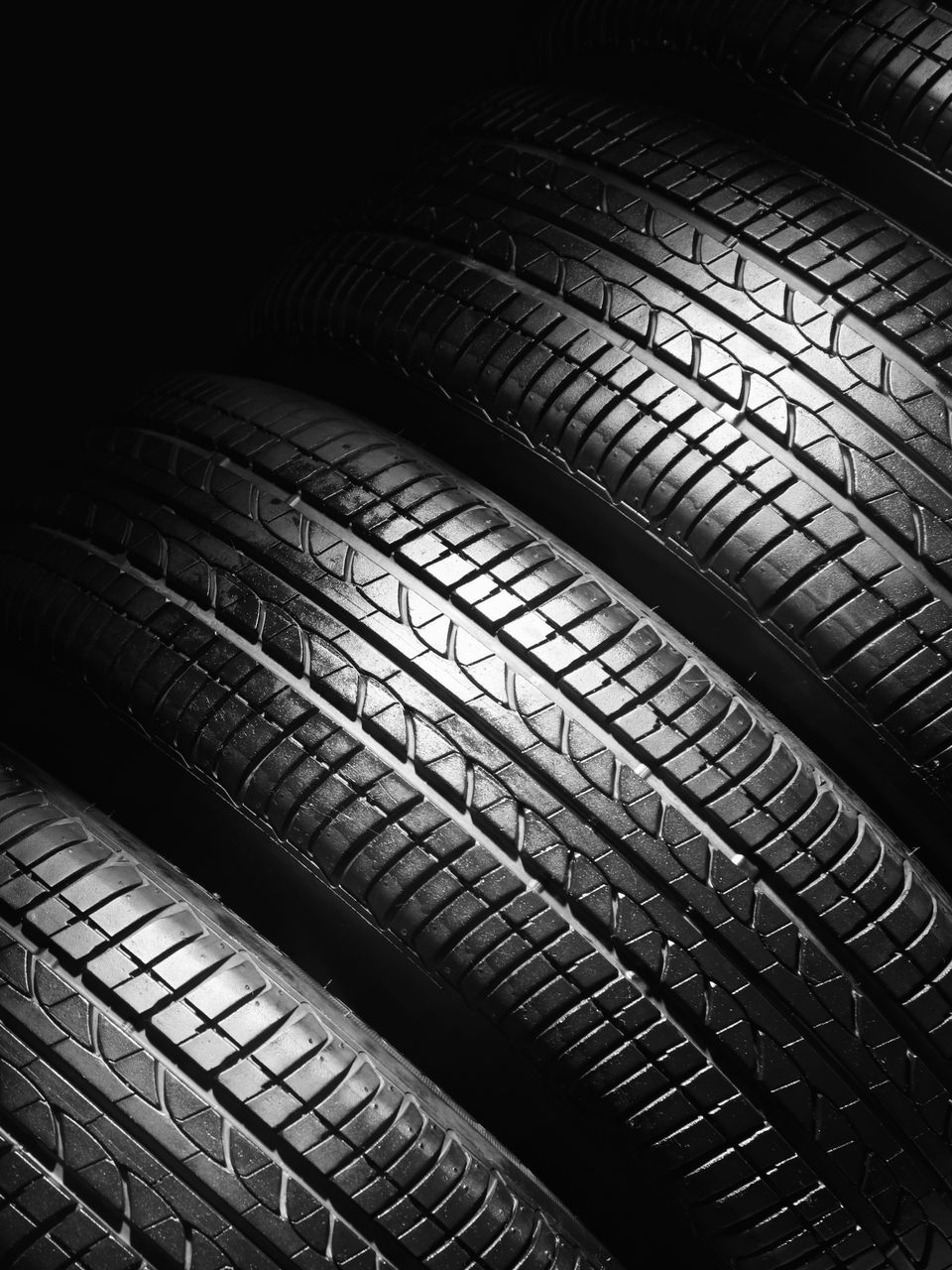 Vue rapprochée en plongée de plusieurs pneus noirs de véhicules empilés, mettant en valeur leurs sculptures sous un éclairage spectaculaire.