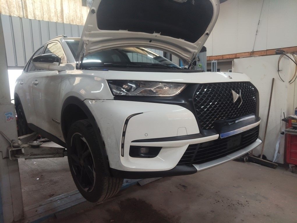 Un SUV DS blanc, capot ouvert, est surélevé sur un pont élévateur dans un atelier automobile lumineux.